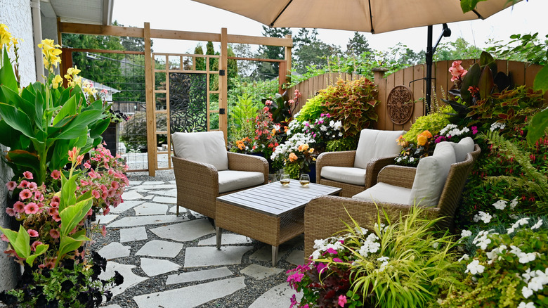 Patio with seating area, lush flowers, and stone pavers.