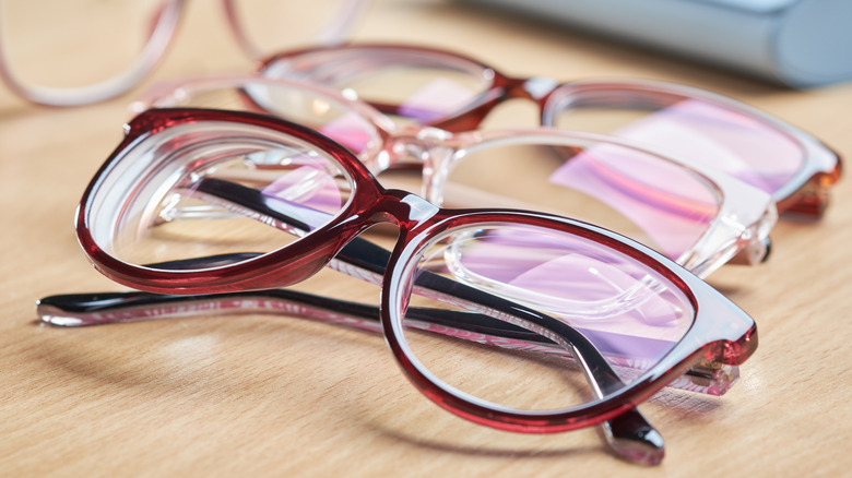 Several plastic eyeglasses in similar shapes but different color lying faceup on a wooden table