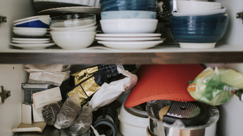 A cluttered cabinet with dishes, placemats, and baking items