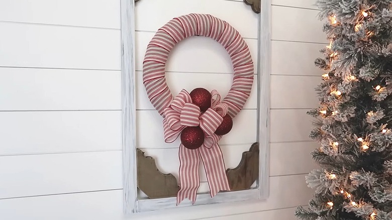 Pool noodle wreath wrapped in striped ribbon with bows and ornaments hanging on a wall near a tree