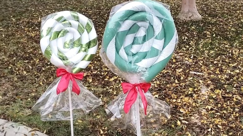 Two green and white giant lollipops made from spiraled pool noodles with plastic wrap and red bows