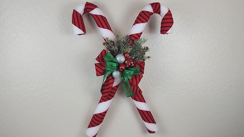 Giant criss-crossing candy canes made from white pool noodles and red ribbon with bows, florals, and ornaments in the middle