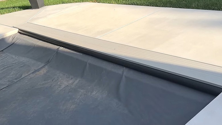 Black pool noodle tucked into a pool cover vault to block leaves