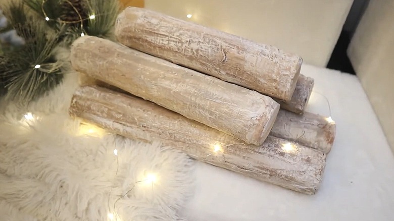 Birch logs made out of pool noodles next to white furry fabric with fairy lights wrapped around them