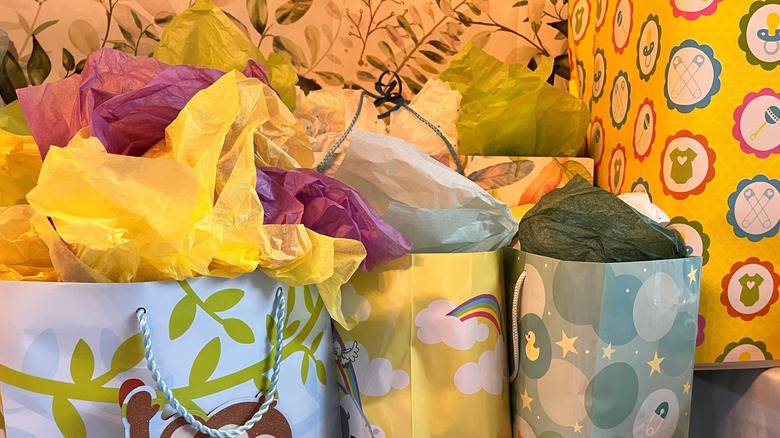 Gift bags topped with purple, yellow, green and white tissue paper stand on a table.