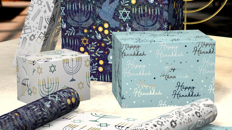 Four gifts wrapped in hanukkah wraping paper with a hanukkah candle lit behind them