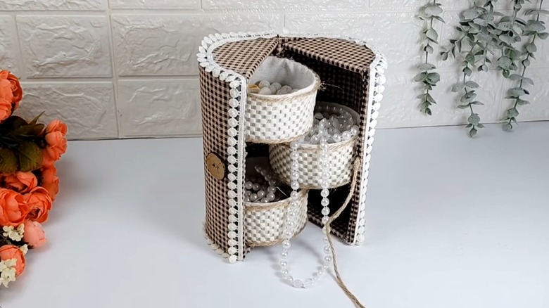 Decorated tuna cans are part of an upcycled storage container covered in fabric.