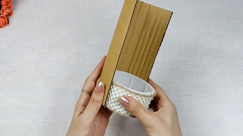 A pair of hands curve a piece of cardboard around a decorated tuna can.