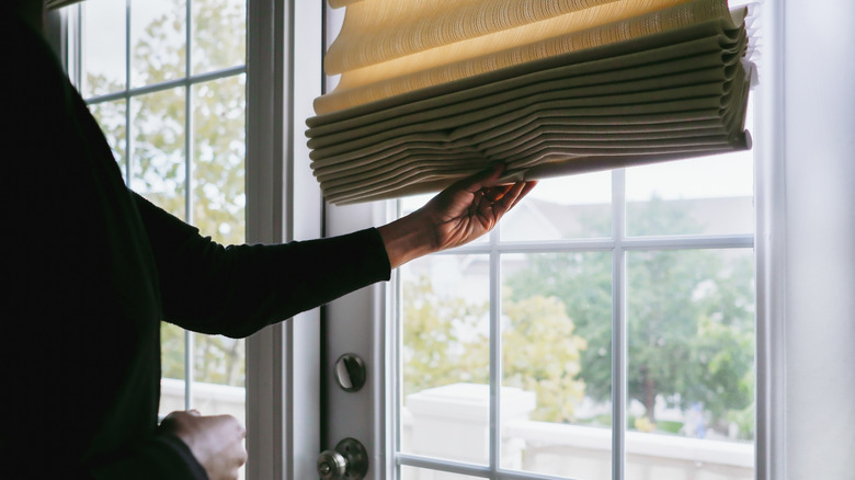 Close-up of someone adjusting Roman shades on French door