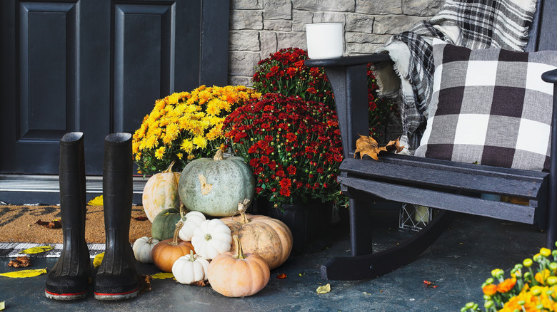 Rain boots, pumpkins, and mums on a fall-themed front porch