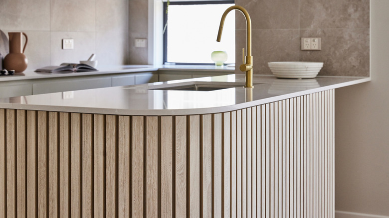 A curved kitchen wooden countertop with sink and gold tap.