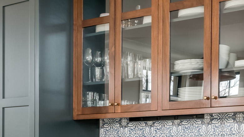 A close up of a glass front kitchen cabinet filled with dishware