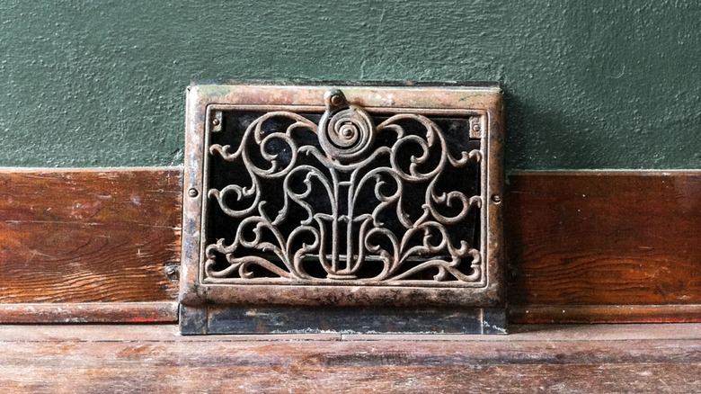 An old vent grate on a dusty baseboard