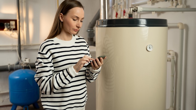 Young woman holding a phone and standing next to boiler