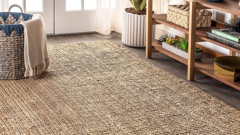Handwoven chunky jute area rug beside wood shelf and decorative basket