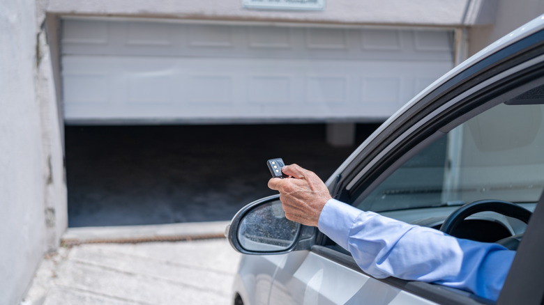 Man in car pointing his garage door remote at an opening garage