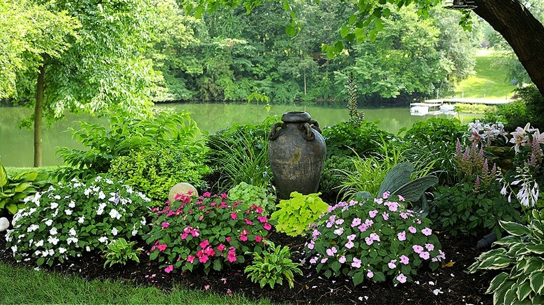 Garden with impatiens flowers in a shady spot near a lake with a tree