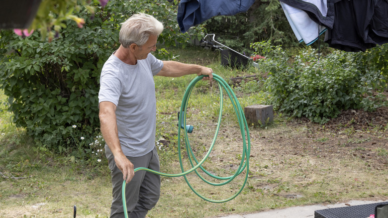 Man coiling a garden hose in garden