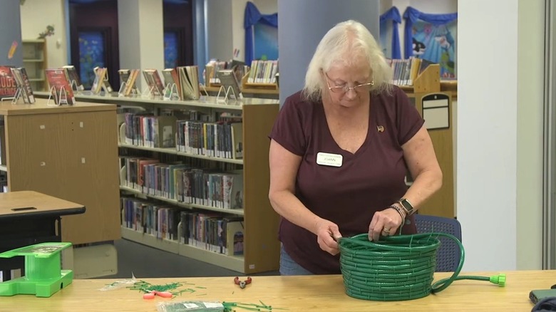 Person making a plant pot out of a garden hose on a table in a library