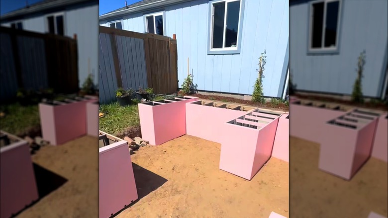 Raised garden beds made out of old file cabinets and painted pink arranged in a residential backyard.