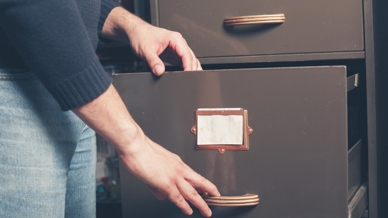 A person pulls out a drawer of an old empty file cabinet.