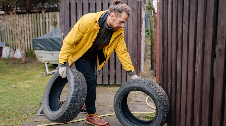 Man holding two old tires outside by fence