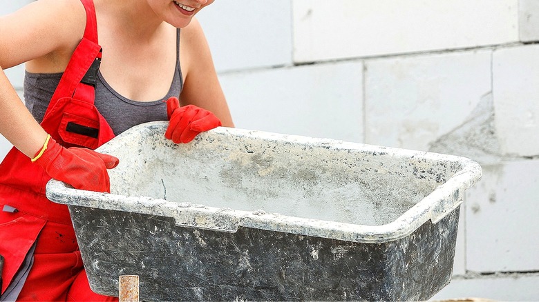 Person in red overalls leaning over a square tub full of mixed concrete