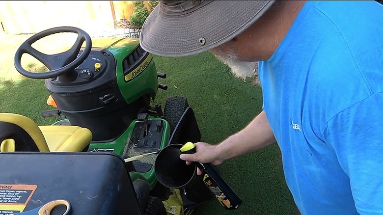 A gardener sprays the inside of a lawn mower's bagging chute with car wax.