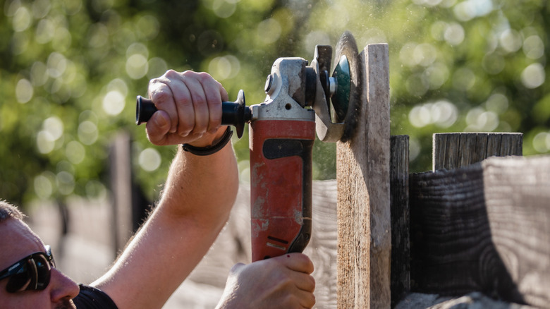 A person using an angle grinder to clean up a fence post.