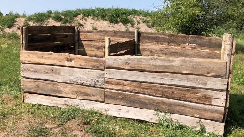 A hand-built wooden compost bin with two compartments in an expansive backyard.