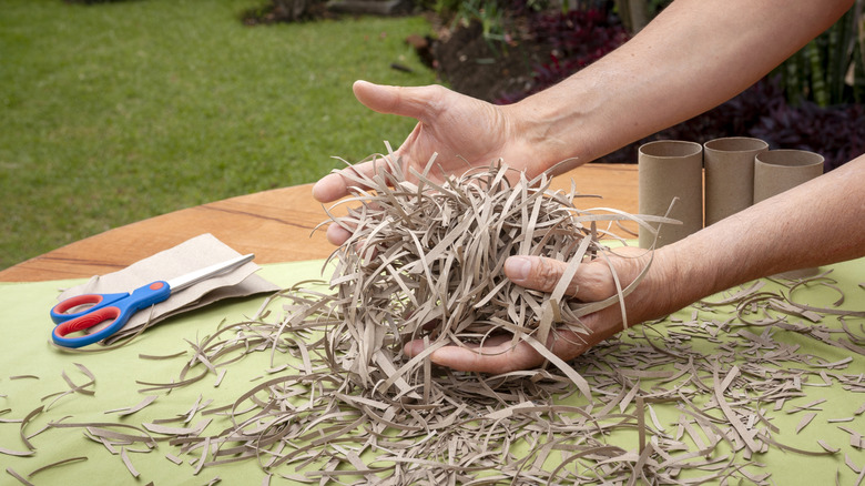 Two hands hold a pile of cut up toilet paper tubes on a table in a garden.