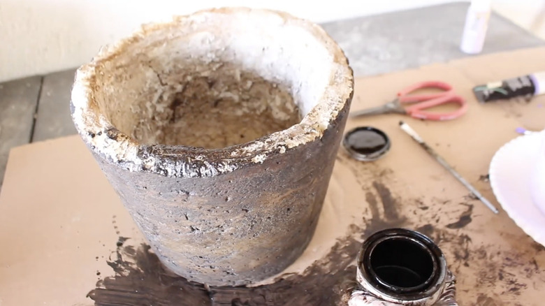 A large papercrete planter its on a table next to a tub of brown paint.