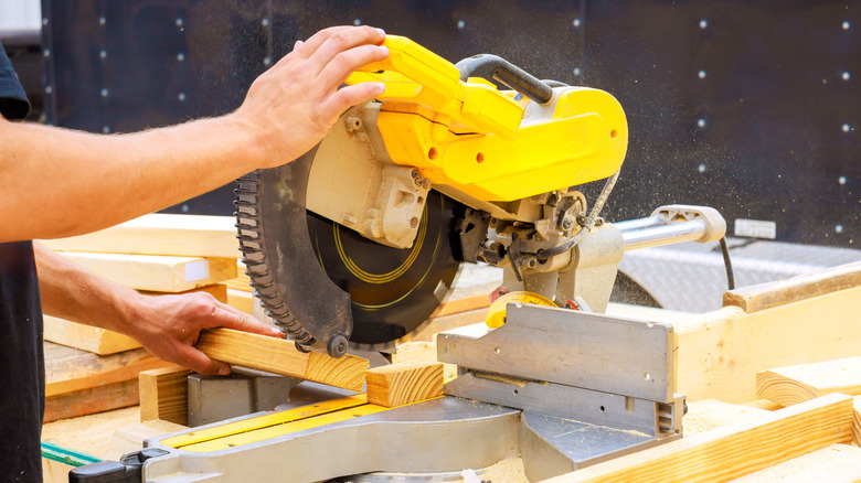 A man cutting planks of wood with a miter saw