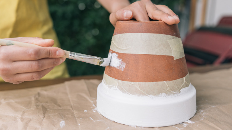 Person in a yellow apron painting an upside down terracotta pot white