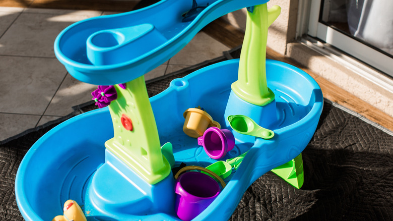 A blue and green plastic kids water table on the back patio of a house.