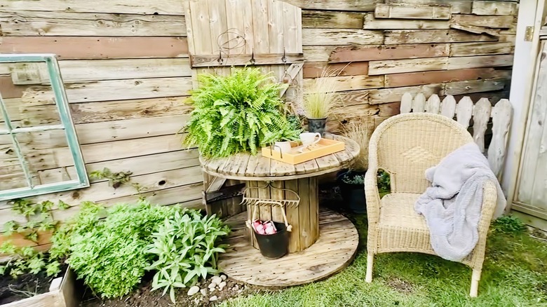 Cable school in garden with garden-rake top for hanging storage, accessorized with plants, chair, beverages, and a panel backdrop behind the table.