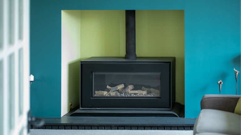A large gas fireplace is surrounded by a bright teal wall