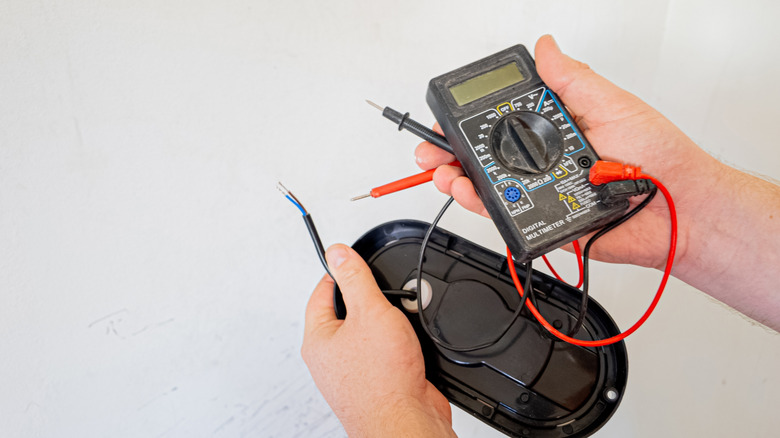 Hands are shown holding a digital multimeter tool