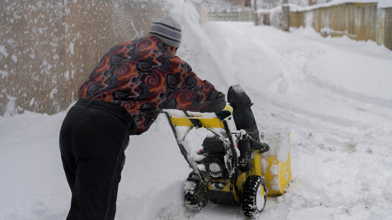 Person pushing snowblower up incline