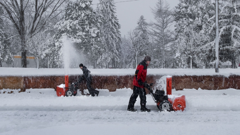 Two people pushing snowblowers in opposite directions