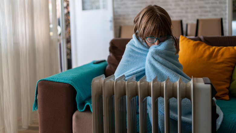 a young girl trying to keep warm near a heating radiator