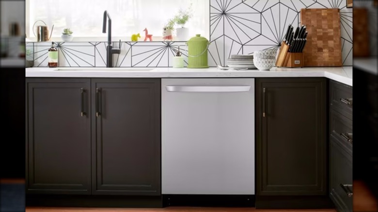 A stainless steel LG dishwasher is surrounded by black kitchen countertops and a modern black and white backsplash