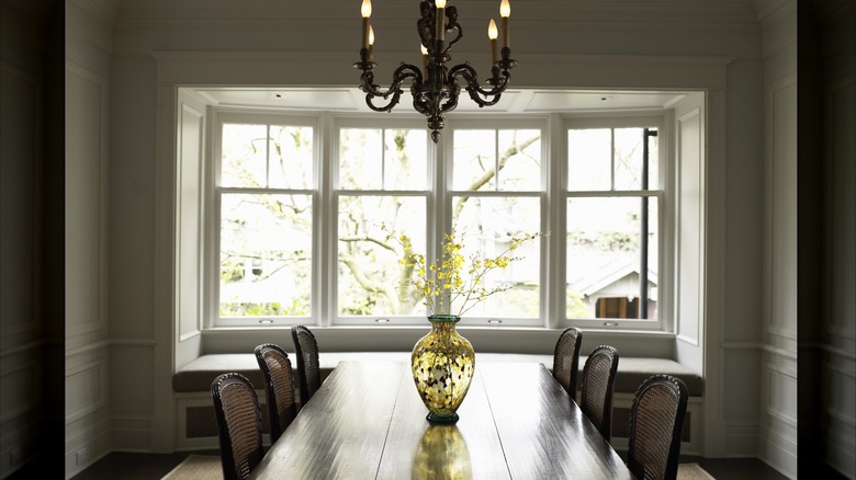 A formal dining room in front of a bay window with a large chandelier.