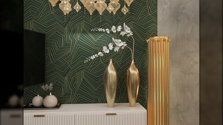 Gold accented decor pieces sitting on a side table with geometric gold and green wallpaper in the background.