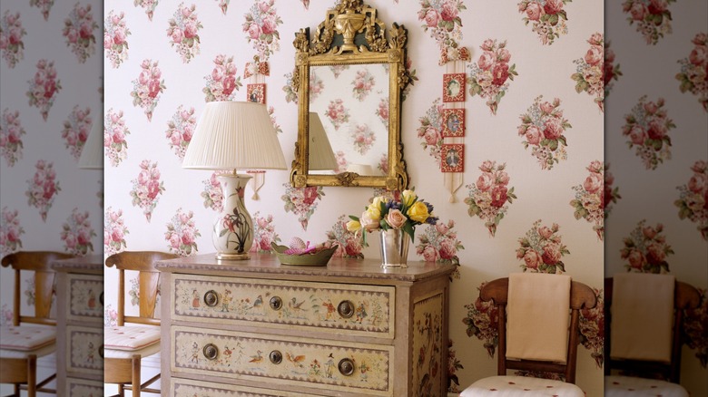 A room with floral wallpaper and floral accented furniture in it.
