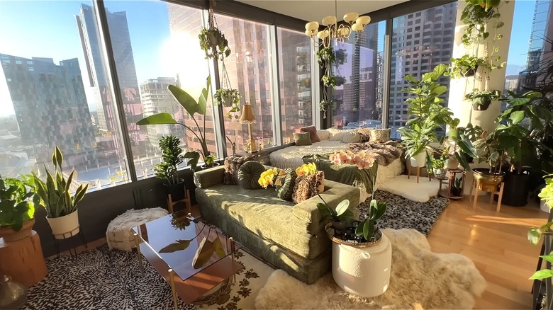 Bright window-clad penthouse loft apartment with a green couch, white bed, and an abundance of greenery throughout.