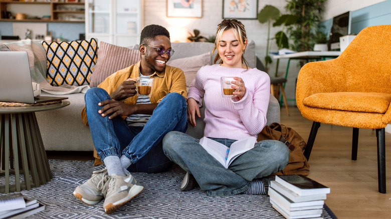 Students doing their school tasks at home together, sitting on floor while having a coffee.