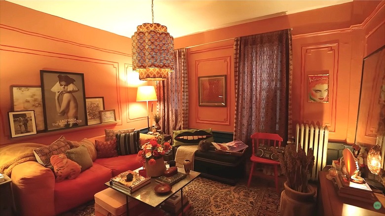 An eclectic living room with peach walls, colorful couches, statement lamp, and multiple posters on the walls.