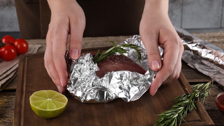 hands wrapping meat in aluminum foil