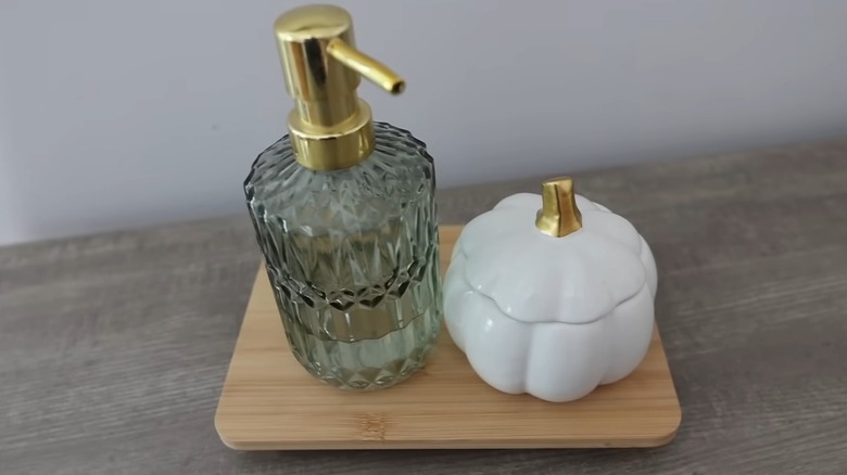 A soap dispenser and white dish on a bamboo riser